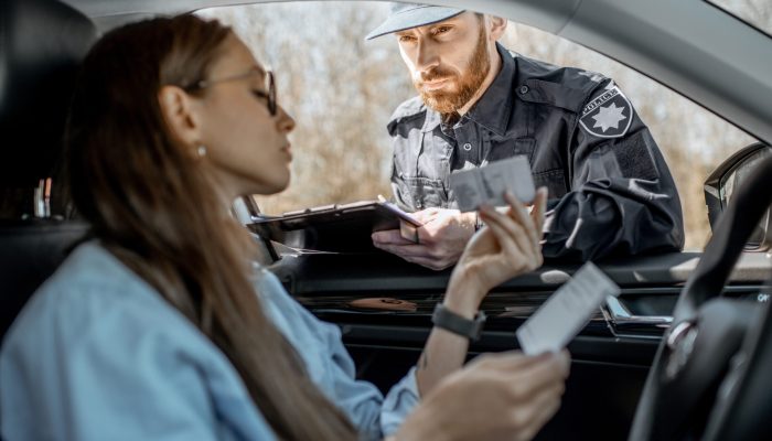 Policeman checking documents of a young female driver sitting in the car, view from the car interior